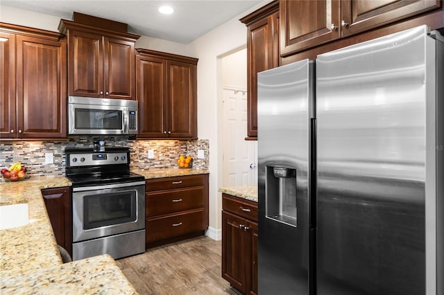 kitchen with tasteful backsplash, appliances with stainless steel finishes, light wood-style flooring, and light stone counters