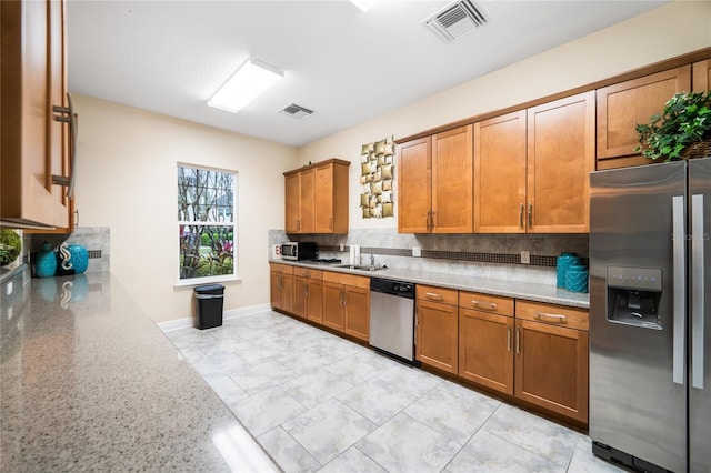 kitchen with appliances with stainless steel finishes, brown cabinets, visible vents, and light stone countertops