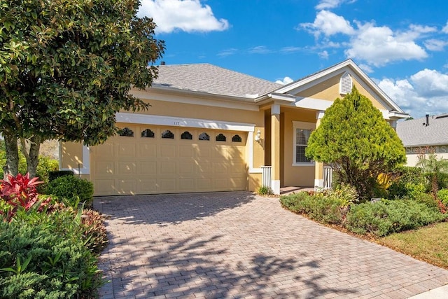 ranch-style house featuring decorative driveway, roof with shingles, an attached garage, and stucco siding