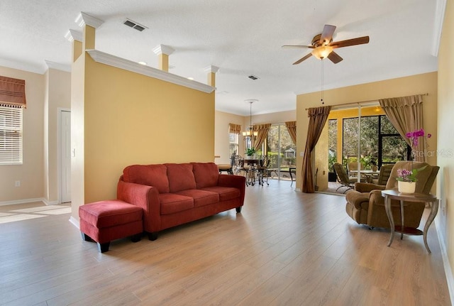 living room featuring visible vents, crown molding, light wood finished floors, and ceiling fan with notable chandelier