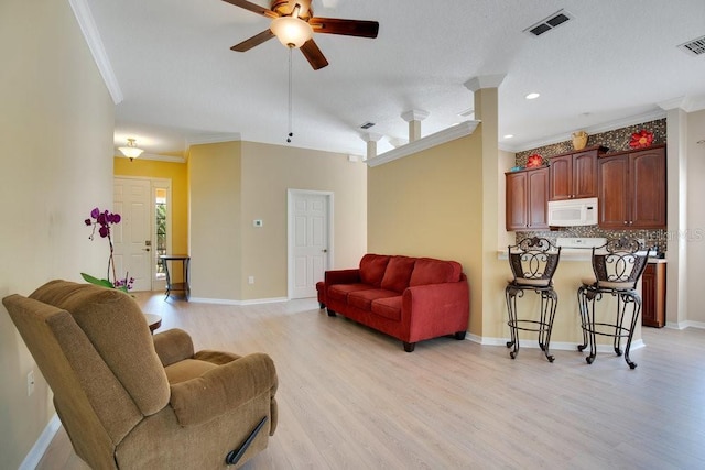 living room with ornamental molding, visible vents, light wood-style floors, and baseboards