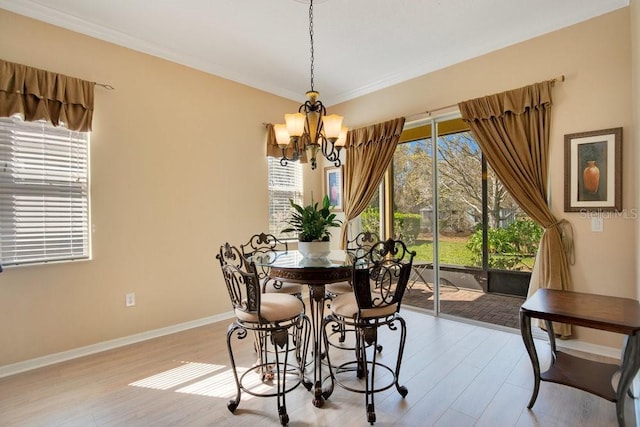 dining area featuring a chandelier, ornamental molding, light wood-type flooring, and baseboards