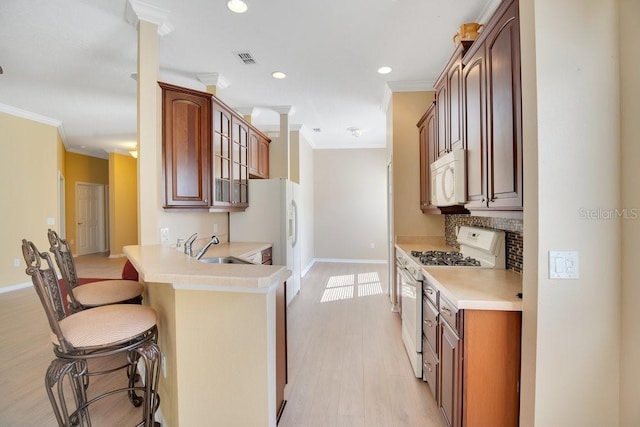 kitchen featuring a breakfast bar area, light countertops, glass insert cabinets, a sink, and white appliances