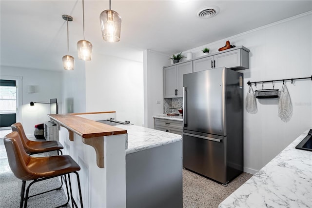 kitchen with light speckled floor, gray cabinets, visible vents, freestanding refrigerator, and light stone countertops