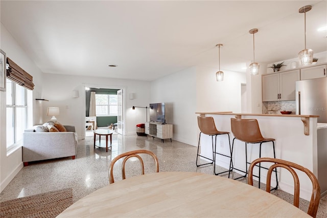 dining room featuring light speckled floor, plenty of natural light, and baseboards