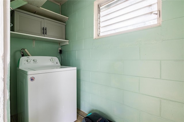laundry room featuring concrete block wall, cabinet space, and washer / clothes dryer
