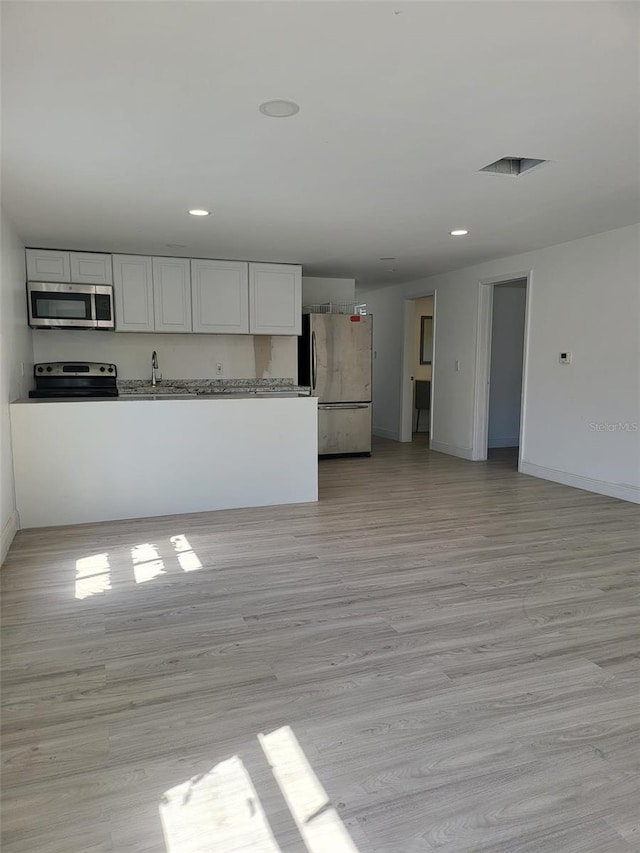 kitchen featuring light wood-style flooring, stainless steel appliances, baseboards, open floor plan, and white cabinets