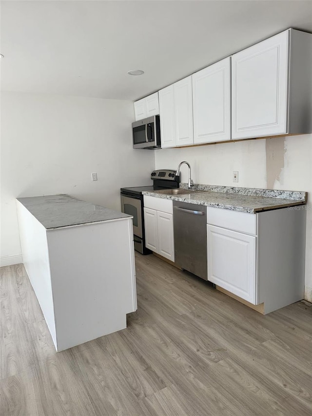 kitchen with stainless steel appliances, light countertops, light wood-style floors, white cabinets, and a sink