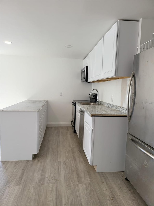 kitchen featuring light countertops, light wood-style flooring, appliances with stainless steel finishes, white cabinets, and baseboards