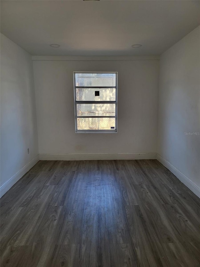 spare room featuring dark wood-style floors and baseboards