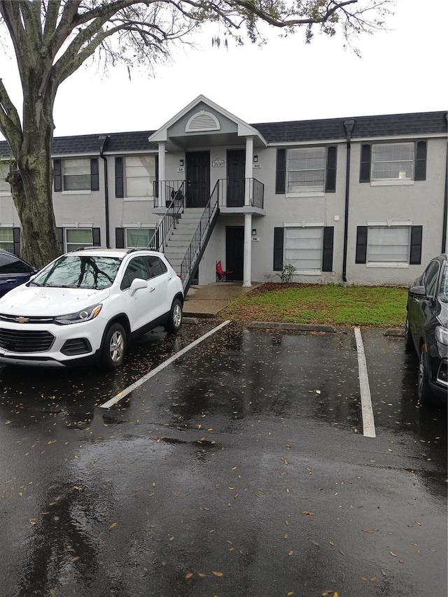 view of front of home with uncovered parking, stairway, and stucco siding