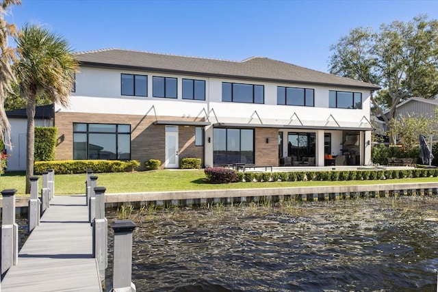 rear view of property featuring stucco siding, a water view, and a yard