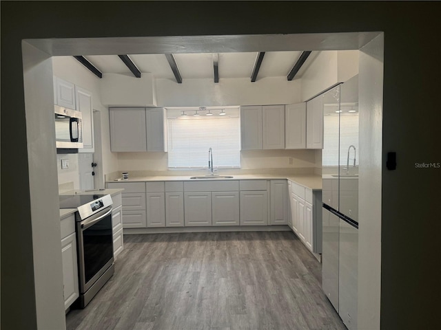 kitchen with stainless steel appliances, beam ceiling, a sink, and light wood-style flooring