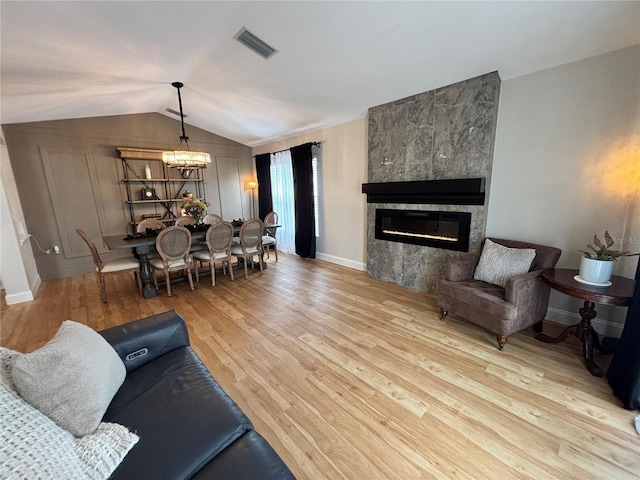 living area with a notable chandelier, lofted ceiling, visible vents, a tiled fireplace, and light wood-style floors