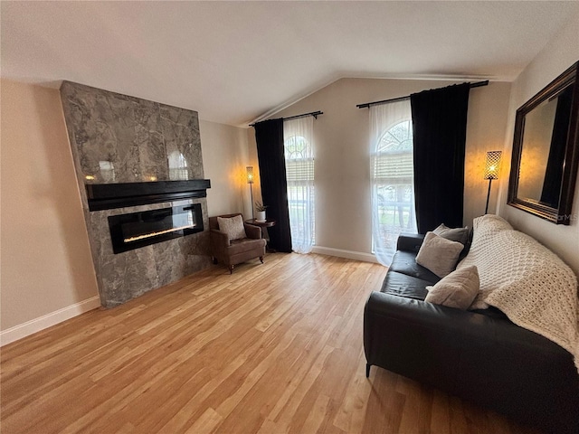 living room with light wood-type flooring, baseboards, a tiled fireplace, and lofted ceiling