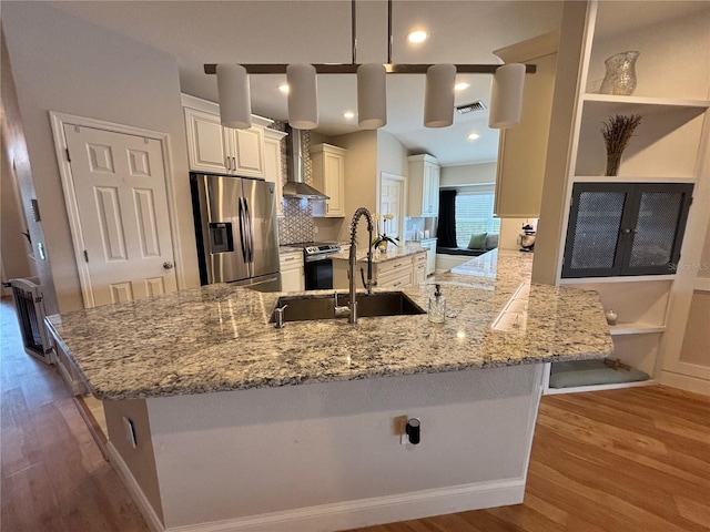 kitchen with a peninsula, a sink, appliances with stainless steel finishes, wall chimney exhaust hood, and decorative light fixtures