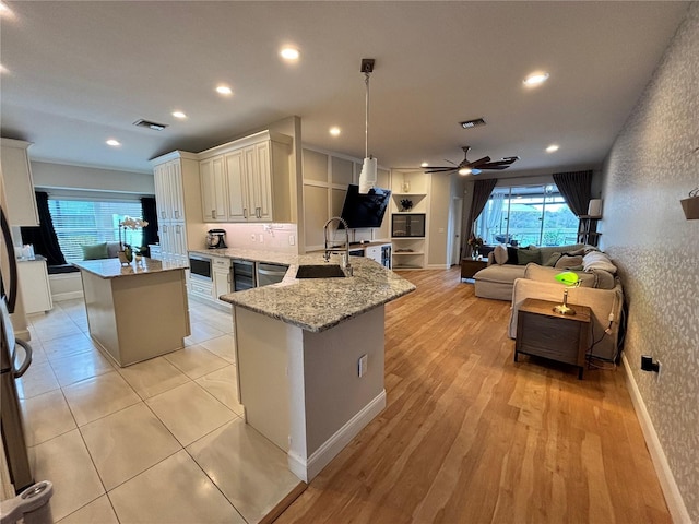 kitchen featuring a center island, hanging light fixtures, light stone countertops, a peninsula, and a sink