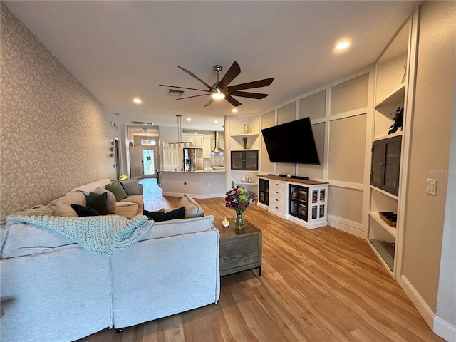 living room featuring light wood finished floors, visible vents, a ceiling fan, an accent wall, and wallpapered walls