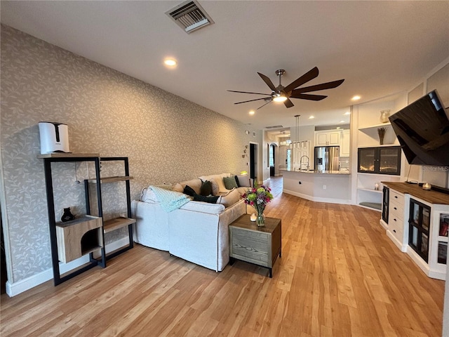 living area featuring visible vents, light wood-style flooring, baseboards, and wallpapered walls