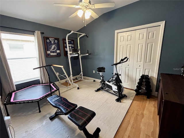 exercise area featuring light wood finished floors, baseboards, vaulted ceiling, and a ceiling fan