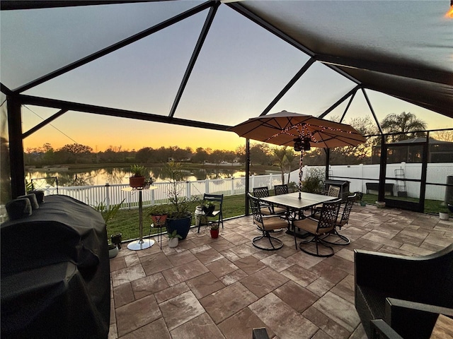 patio terrace at dusk with a water view, a fenced backyard, a lanai, and area for grilling