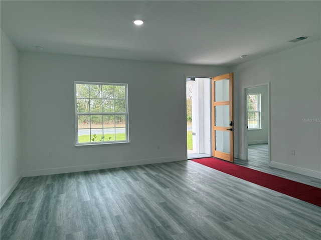 empty room featuring plenty of natural light, wood finished floors, visible vents, and baseboards