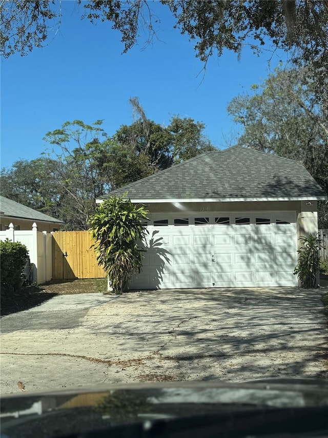 view of property exterior featuring a garage, roof with shingles, an outbuilding, and fence