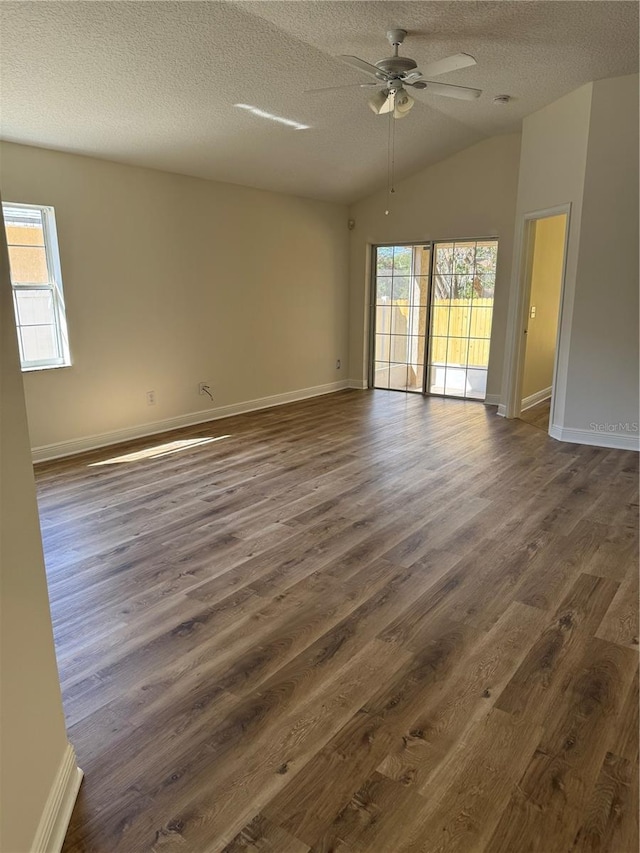 empty room with dark wood finished floors, vaulted ceiling, a textured ceiling, ceiling fan, and baseboards