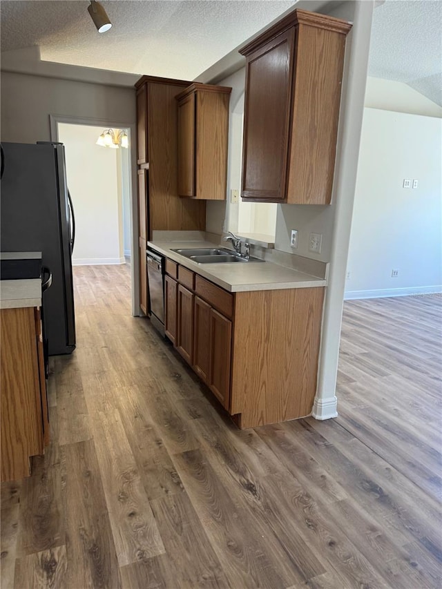 kitchen with freestanding refrigerator, a sink, a textured ceiling, light wood-type flooring, and dishwasher