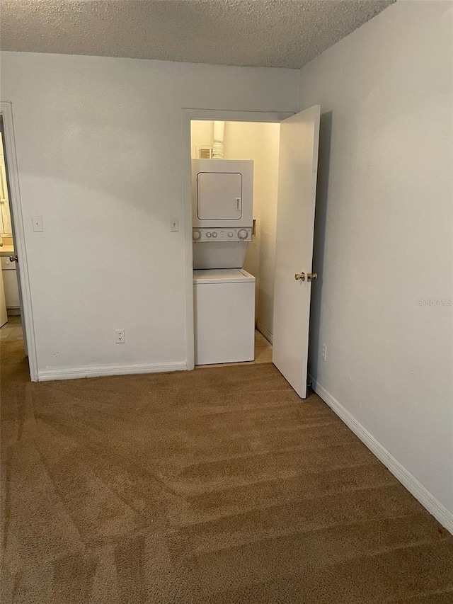 carpeted spare room with a textured ceiling, baseboards, and stacked washer / drying machine