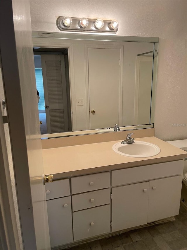 bathroom with toilet, a textured wall, and vanity