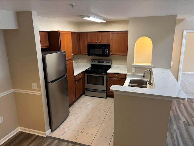 kitchen featuring appliances with stainless steel finishes, brown cabinetry, light countertops, and a sink