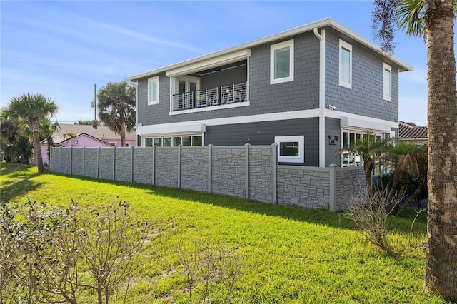 back of property with a yard, stone siding, fence, and a balcony