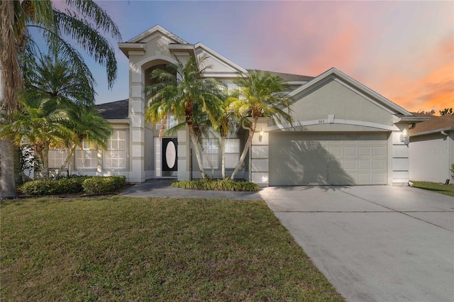 view of front of property featuring concrete driveway, a lawn, an attached garage, and stucco siding