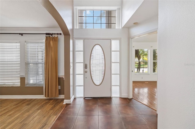 entryway with baseboards, arched walkways, and dark wood-style flooring