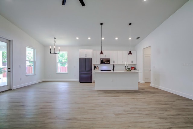 kitchen with a kitchen island with sink, light wood-style flooring, white cabinetry, freestanding refrigerator, and stainless steel microwave