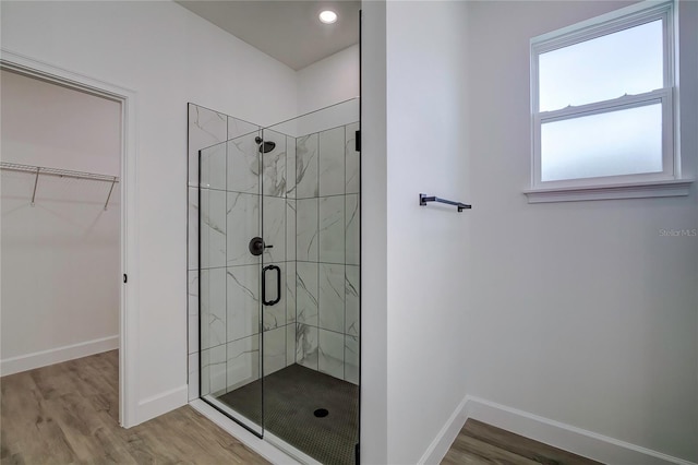 full bath with wood finished floors, a shower stall, baseboards, and a spacious closet