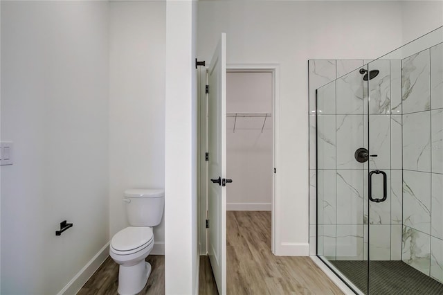 bathroom with a spacious closet, toilet, a stall shower, wood finished floors, and baseboards