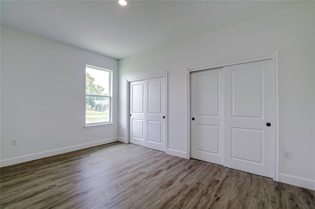 unfurnished bedroom featuring wood finished floors, baseboards, and two closets