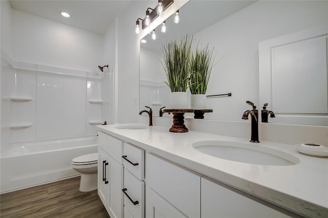 bathroom featuring toilet, double vanity, a sink, and wood finished floors