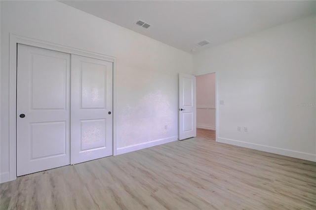 unfurnished bedroom featuring light wood-style floors, baseboards, visible vents, and a closet