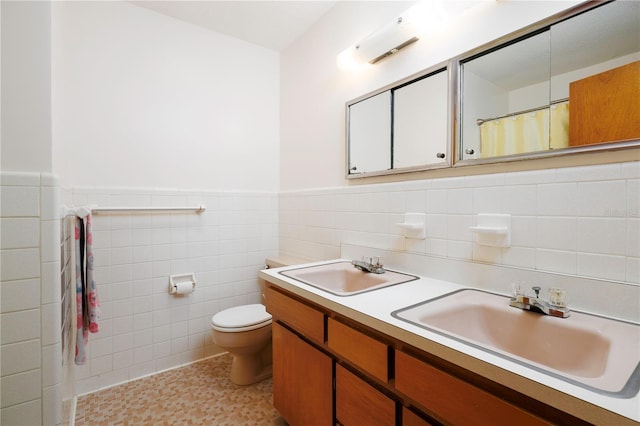 full bath with a wainscoted wall, double vanity, a sink, and toilet