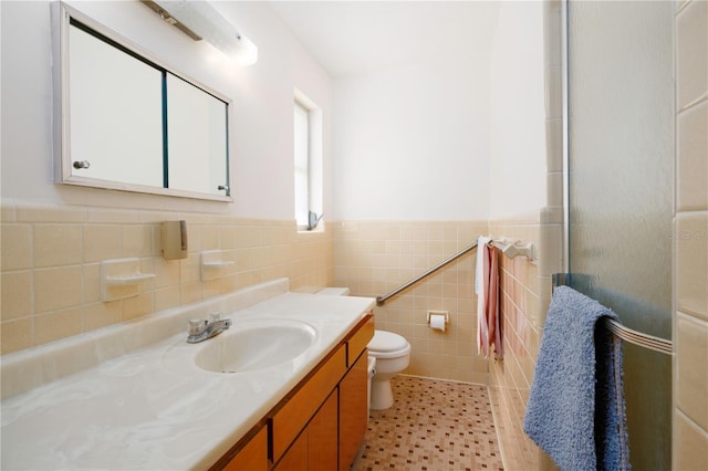 bathroom with toilet, a shower with shower door, a wainscoted wall, vanity, and tile walls