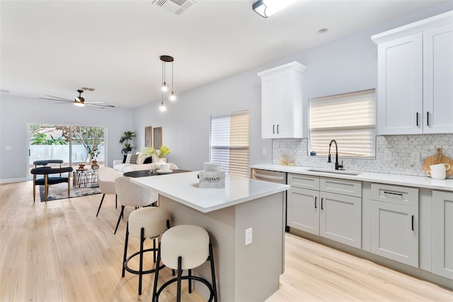 kitchen featuring visible vents, a center island, decorative light fixtures, light countertops, and a sink