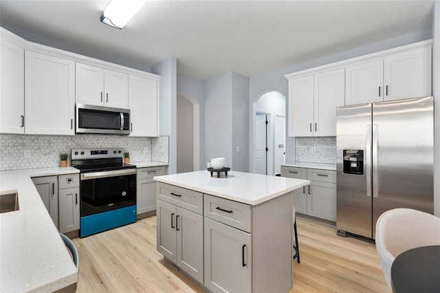 kitchen featuring arched walkways, stainless steel appliances, a kitchen island, white cabinetry, and light wood finished floors