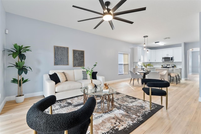 living room with light wood-type flooring, ceiling fan, and baseboards