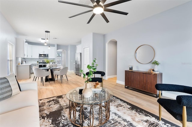 living room featuring light wood-style floors, baseboards, arched walkways, and ceiling fan