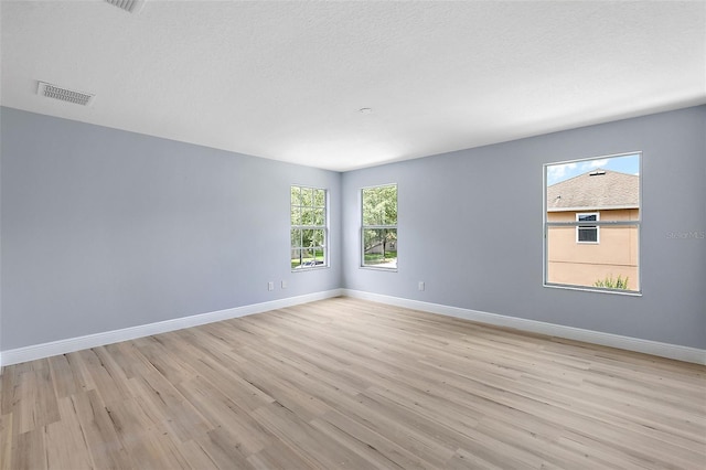 unfurnished room featuring visible vents, light wood-style flooring, baseboards, and a textured ceiling