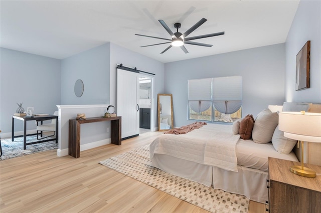 bedroom featuring light wood finished floors, a barn door, a ceiling fan, connected bathroom, and baseboards