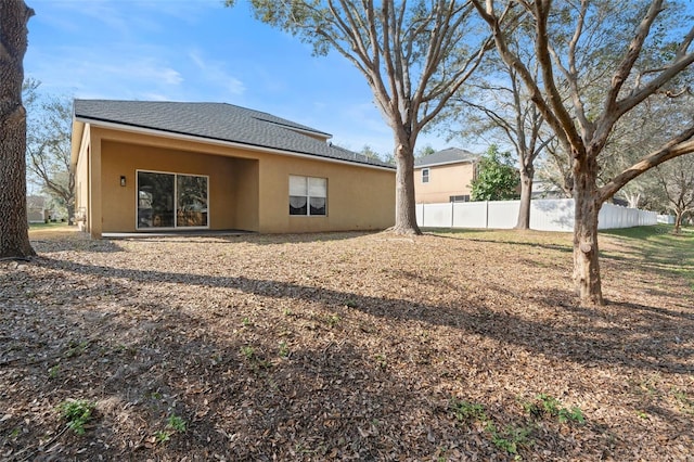 back of property featuring roof with shingles, fence, and stucco siding